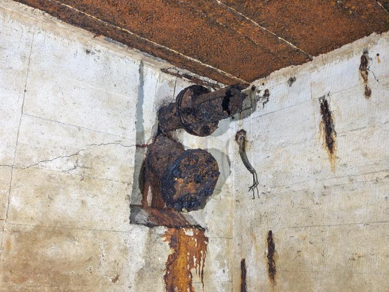 Vue de détail de l'extrémité ouest de la salle de garde : conduit de cheminée (en haut) et conduit de ramonage (en bas) du poêle. Dans le mur, passage de câble électrique du magasin à munitions